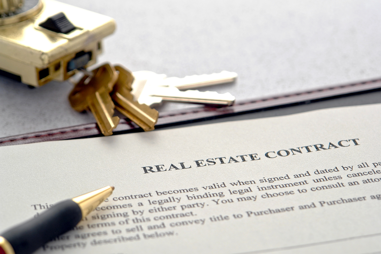 Real estate contract, pen, and house keys sitting on a table.