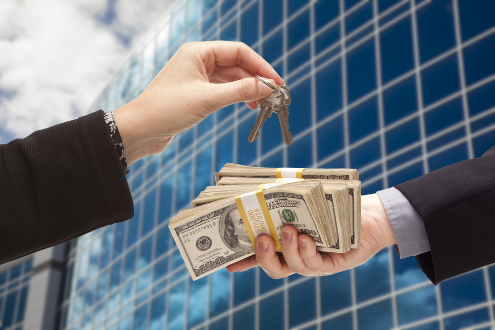 Two hands exchanging cash and keys with glass building in the background. 