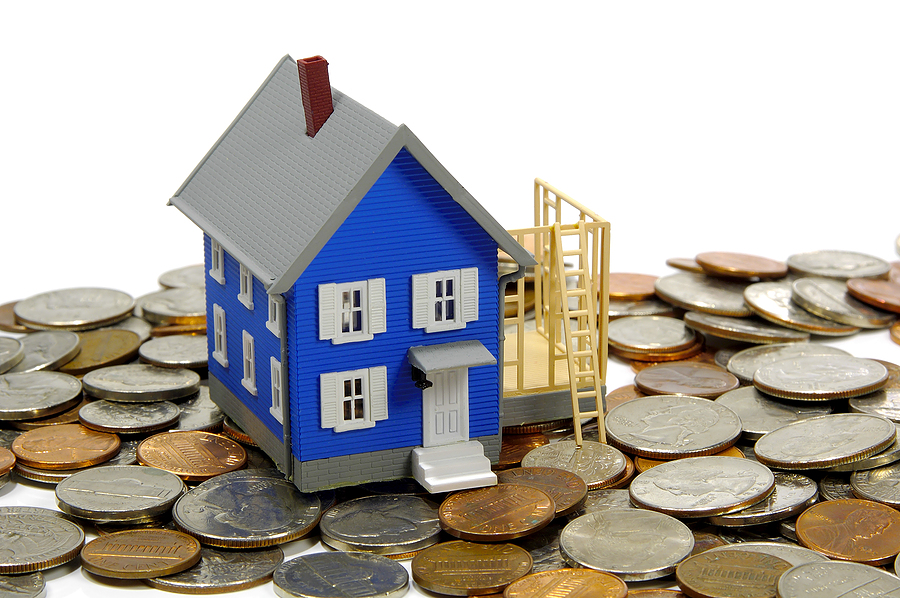 A model blue house with a scaffold sitting on a pile of coins. 