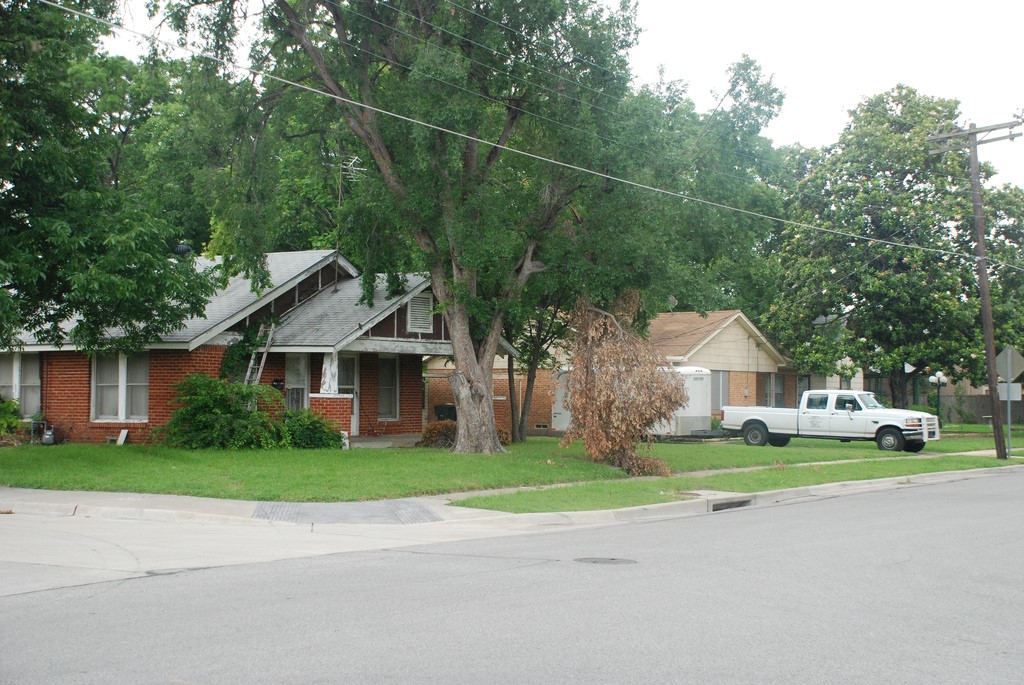 An old, red brick house surrounded by trees in a neighborhood. 