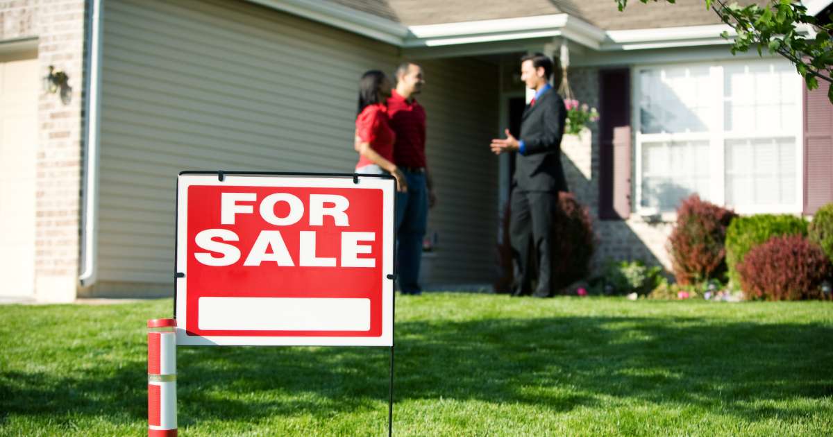 couple talking to agent with for sale sign in yard