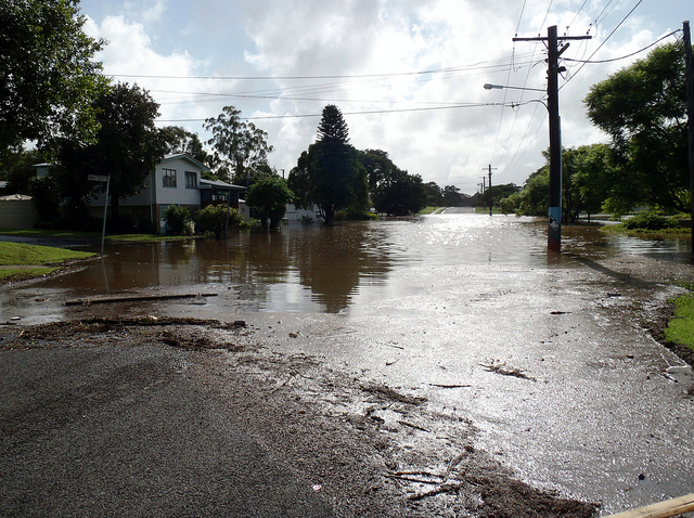 A partially flooded neighborhood street. A two story house stands on the left-hand side.